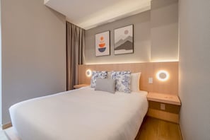 Ein Hotelzimmer mit einem großen Bett, zwei Nachttischen, einem Kopfteil mit integrierter Beleuchtung und zwei an der Wand befestigten Kunstwerken.