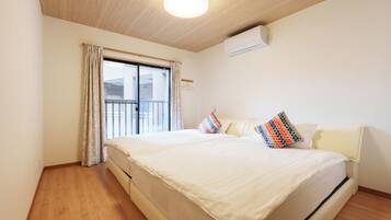 A hotel room with a large bed, a window with curtains, an air conditioning unit, and a wooden floor.