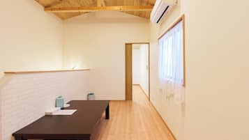 A room with a wooden ceiling, a table with papers, a trash bin, and a window with curtains.