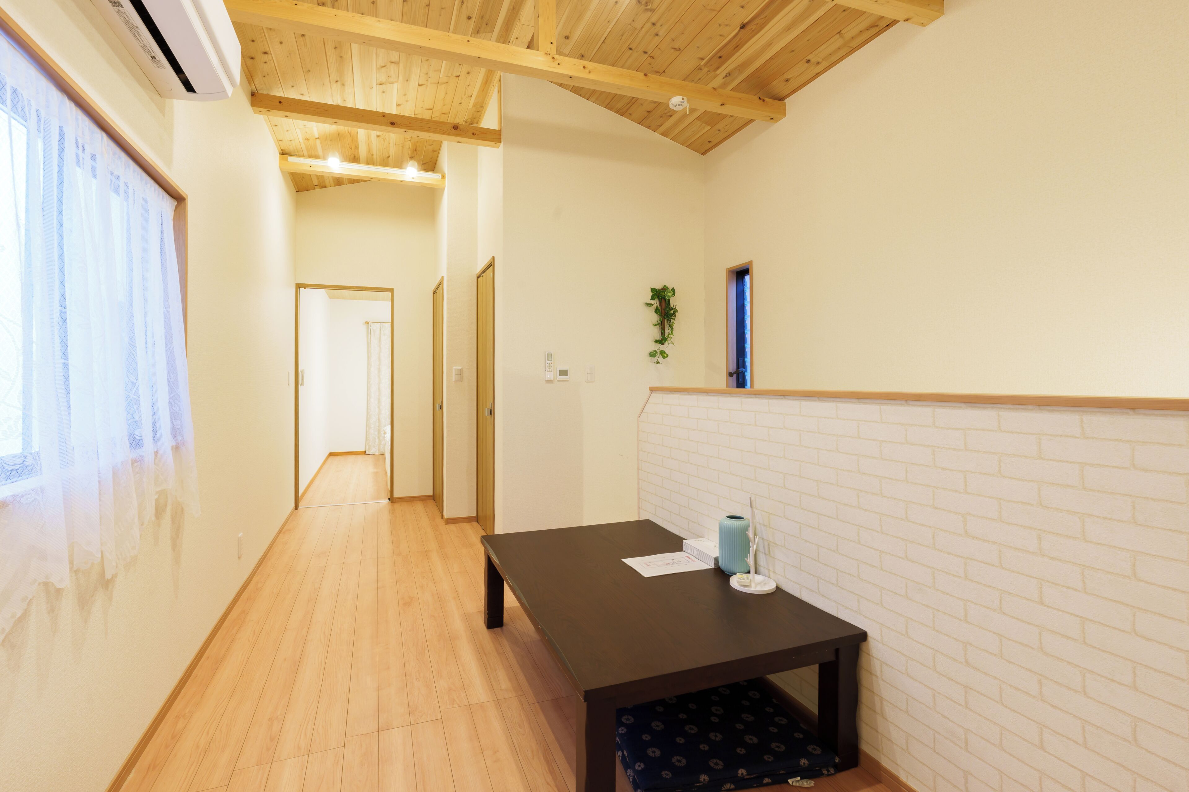 A hallway with wooden flooring, a table with a vase and papers, and a brick-patterned wall.