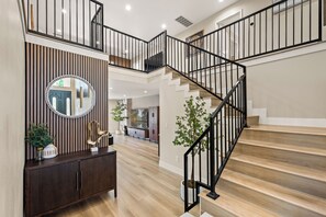 A spacious foyer with a wooden staircase, a large mirror, and a console table with decorative items. - 4500sqft 6BR/7BA/9 Beds/6 Suites/PS5/Texas Hold’em (Rowland Heights)