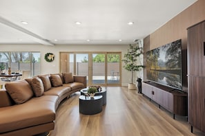 A modern living room with a leather sofa, a coffee table, and a flat-screen TV mounted on a wooden panel wall. - 4500sqft 6BR/7BA/9 Beds/6 Suites/PS5/Texas Hold’em (Rowland Heights)