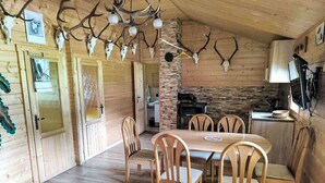 A wooden interior with a dining table and chairs, a fireplace, and antler decorations.