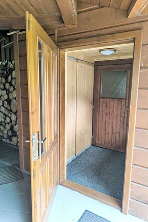 A wooden door with a metal handle, a textured mat at the entrance, and a stack of firewood in the background. - U Jelení obory by Interhome (Velke Karlovice)