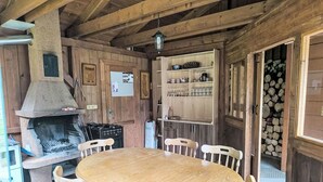 A wooden interior with a round table and chairs, a stone fireplace, and a wooden door with shelves above.