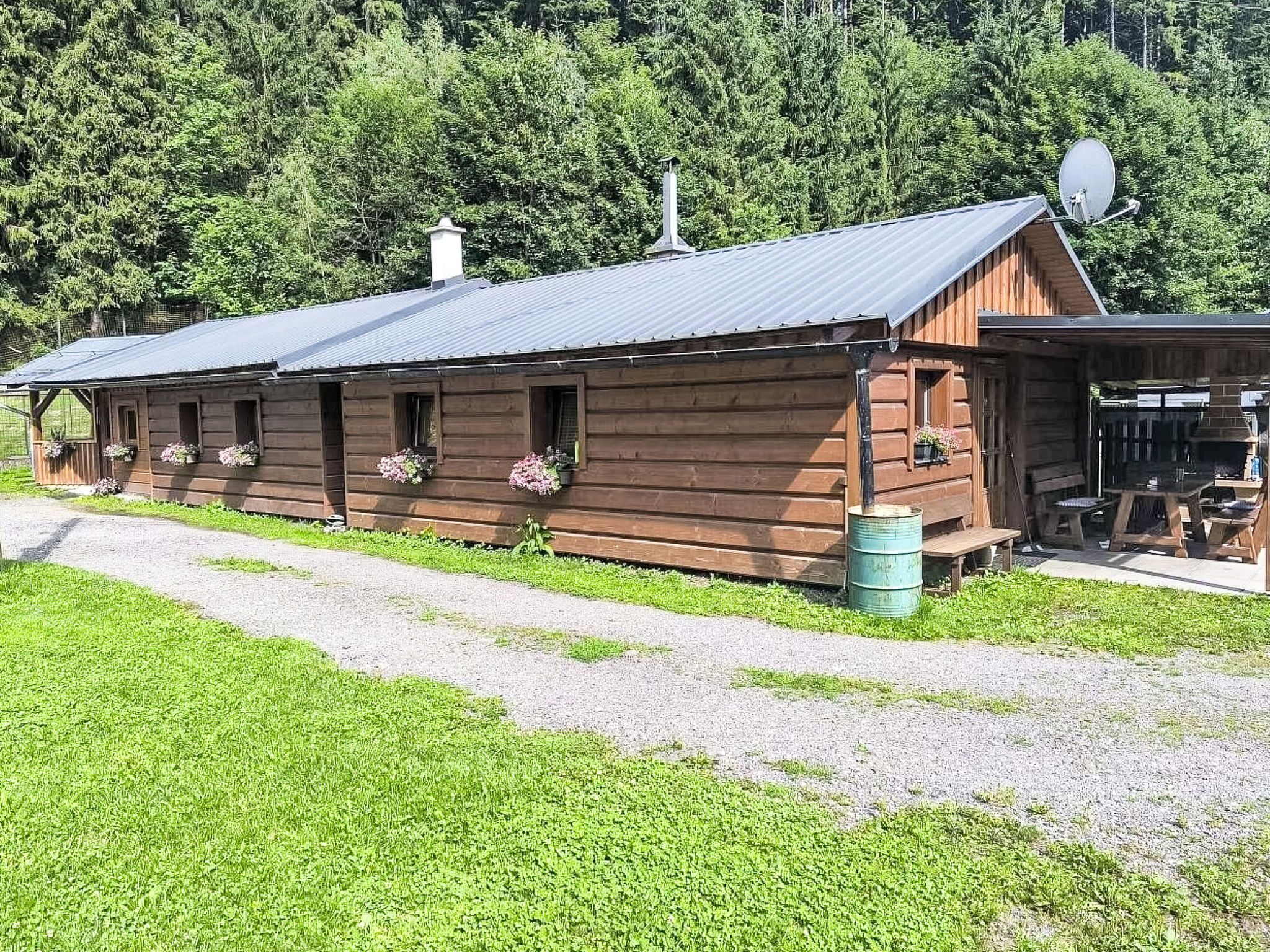 A wooden cabin with a gravel driveway, surrounded by greenery.