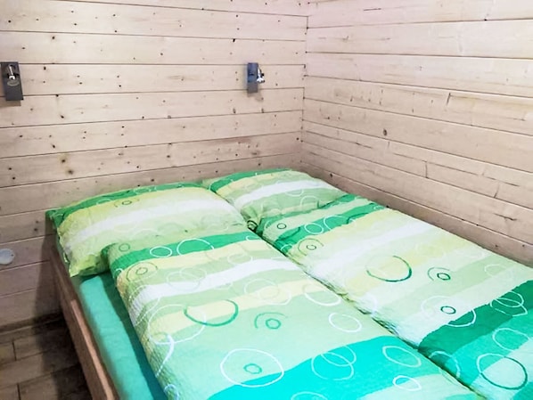 A small, single-bed room with wooden walls and a simple, clean design.