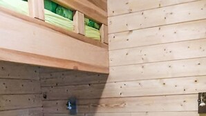 A bunk bed with two levels, wooden walls, and a green patterned bedspread.