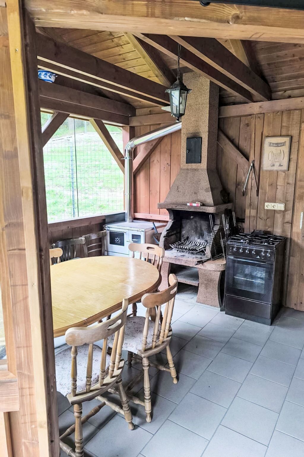 A rustic kitchen with a stone oven, wooden chairs, and a dining table.