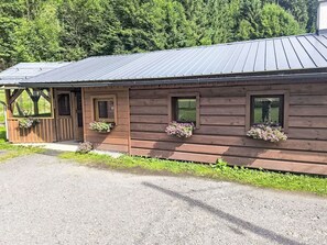 A wooden building with a metal roof, two windows with flower boxes, and a door.