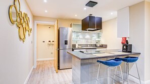 A modern kitchen with a stainless steel refrigerator, a built-in oven, and a bar area with stools. - Hybridresi Battersea - Battersea Park Road (London)