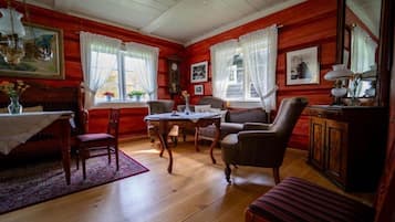 A room with wooden walls, a dining table with chairs, a sofa, a cabinet, and a mirror.