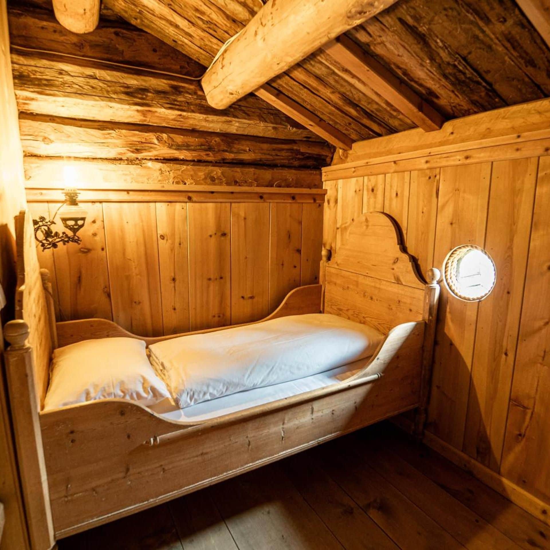 Ein hölzernes Etagenbett mit einer Matratze und Kissen, eine Wandleuchte sowie eine Holzwand mit freiliegenden Balken.