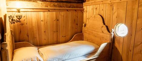Ein hölzernes Etagenbett mit einer Matratze und Kissen, eine Wandleuchte sowie eine Holzwand mit freiliegenden Balken.