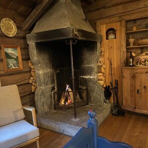 Une cheminée en pierre avec un feu qui crépite à l’intérieur, entourée de murs en bois et d’un banc.
