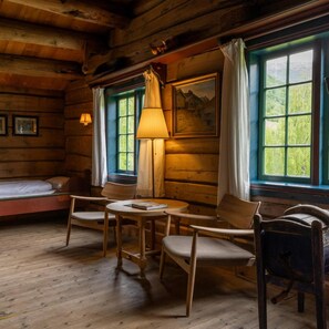 A cozy cabin interior with a wooden floor, a bed, a table with chairs, and a painting on the wall.
