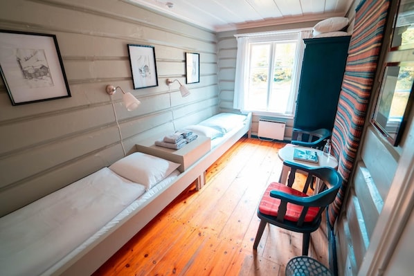 A compact room with a single bed, a small table, a chair, and a window with curtains. - Roisheim Hotell (Lom)