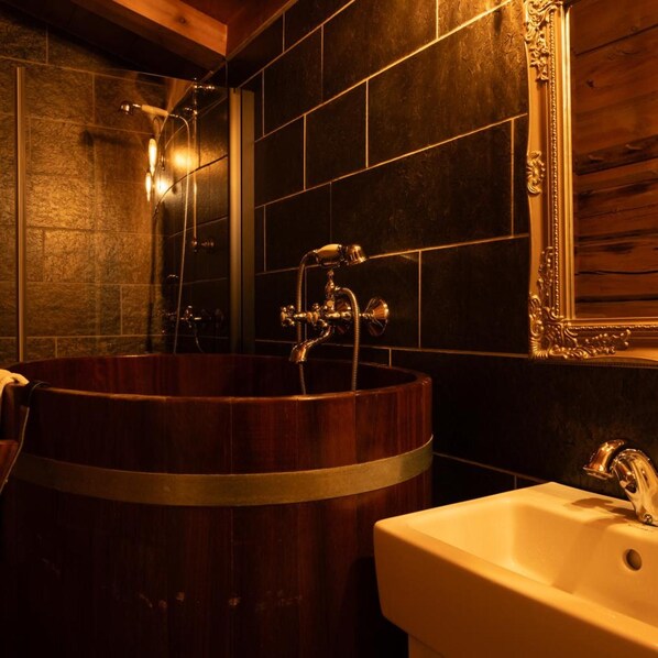 A bathroom with a wooden bathtub, a white sink, and a mirror with an ornate frame. - Roisheim Hotell (Lom)