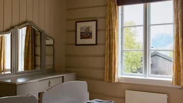 Een hotelkamer met een bed, een kaptafel, een spiegel, een raam met gordijnen en een ingelijst beeld aan de muur.