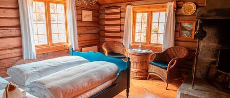 A log cabin bedroom with a bed, two wicker chairs, a small round table, and a fireplace.