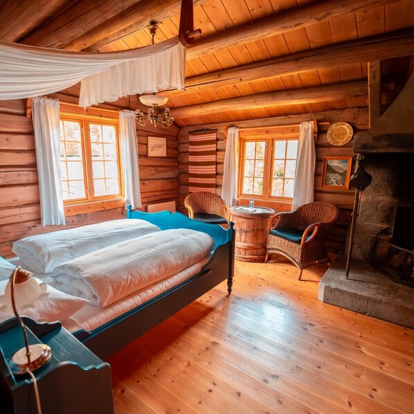 A log cabin bedroom with a bed, two wicker chairs, a small round table, and a fireplace.