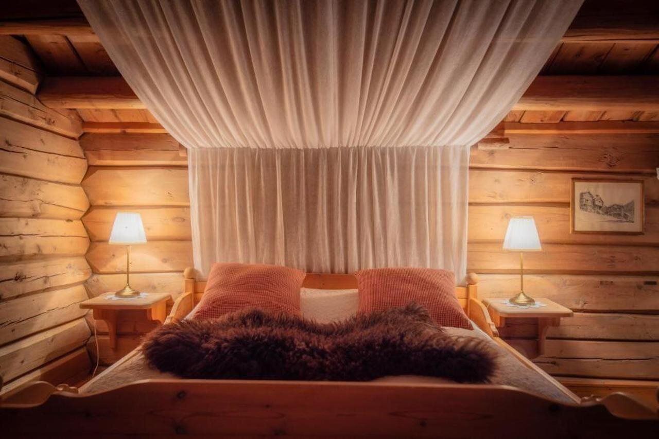 Ett sovrum i en stuga med träpanel, en säng, två sänglampor och en gardin.