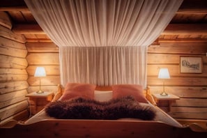 Quarto de cabana de madeira com uma cama, duas luminárias de cabeceira e uma cortina.