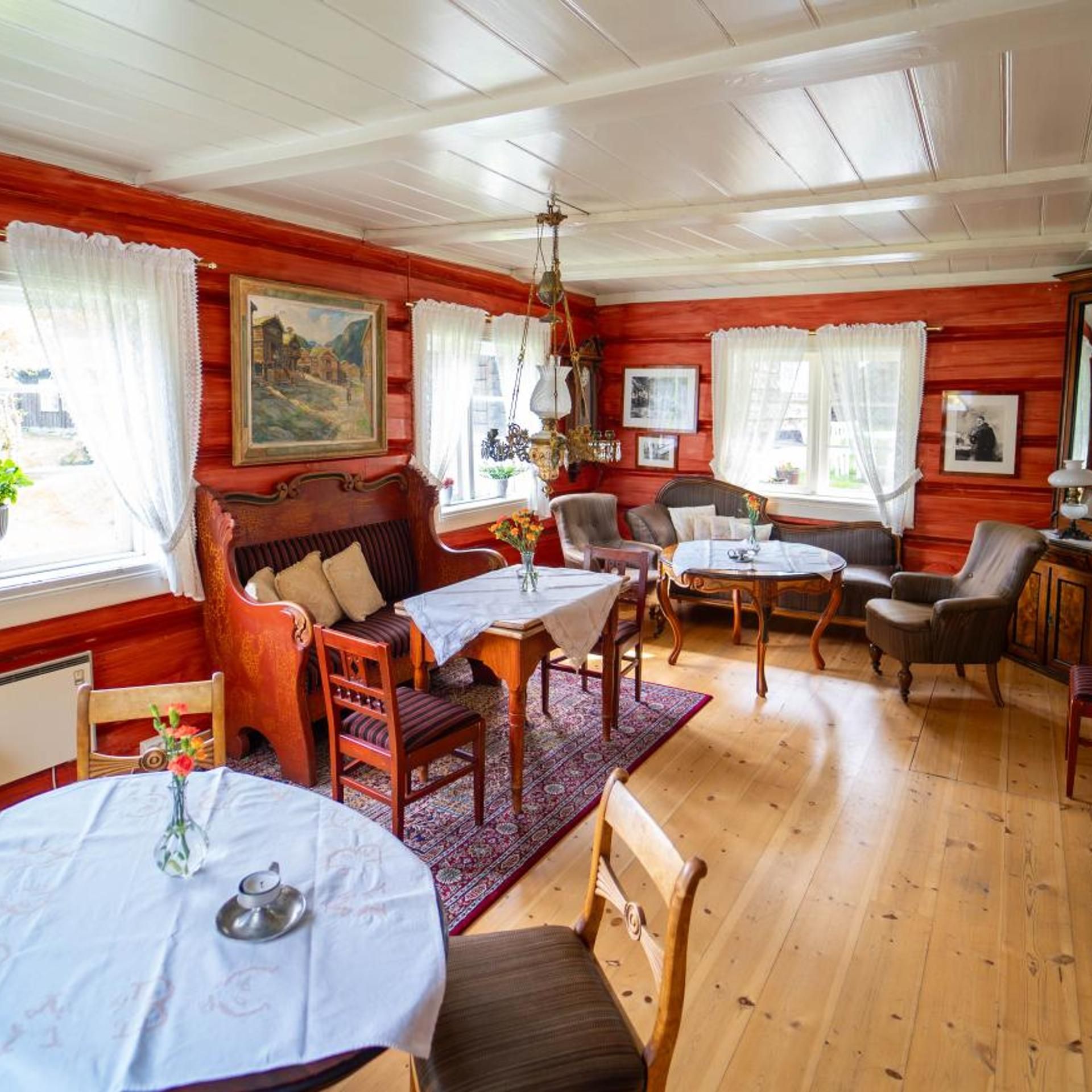 Ein Zimmer mit Holzwänden, einem Esstisch mit Stühlen, einer Couch und einer Pendelleuchte.