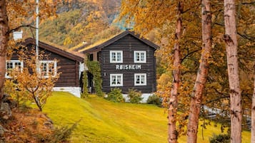 A wooden cabin with the name 'ROISHEIM' on its facade, surrounded by a grassy hillside and trees with autumn foliage.