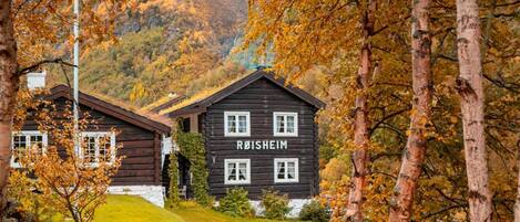 A wooden cabin with the name 'ROISHEIM' on its facade, surrounded by a grassy hillside and trees with autumn foliage.