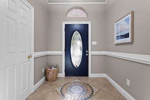 A hallway with a dark blue door, a white door, a wicker basket, a patterned rug, and a framed picture on the wall. - Ocean Springs Bayou Getaway | Outdoor Living (Gulf Park Estates)