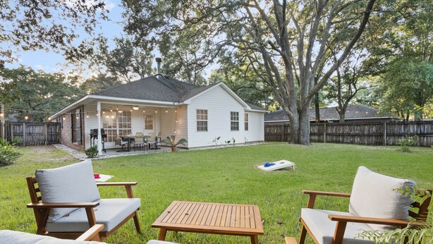 A backyard with a covered patio, a wooden table, and two chairs. - Ocean Springs Bayou Getaway | Outdoor Living (Gulf Park Estates)
