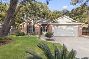 A single-story house with a brick facade, a front garage, and a well-maintained lawn. - Ocean Springs Bayou Getaway | Outdoor Living (Gulf Park Estates)