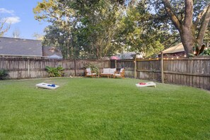 Ein Garten mit Holzzaun, Rasen und einem überdachten Sitzbereich mit Stühlen und Tisch.
