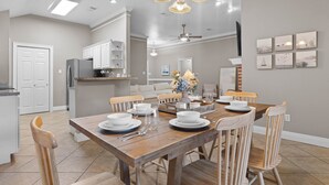 A dining area with a wooden table set for four, surrounded by chairs, in a modern kitchen with white cabinets and a ceiling fan. - Ocean Springs Bayou Getaway | Outdoor Living (Gulf Park Estates)