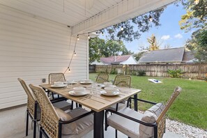 An outdoor patio with a table set for dining, surrounded by wicker chairs with cushions. - Ocean Springs Bayou Getaway | Outdoor Living (Gulf Park Estates)