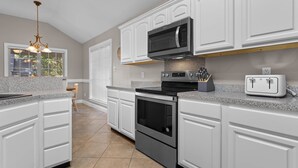 A kitchen with white cabinetry, a stainless steel microwave, a built-in oven, and a granite countertop. - Ocean Springs Bayou Getaway | Outdoor Living (Gulf Park Estates)