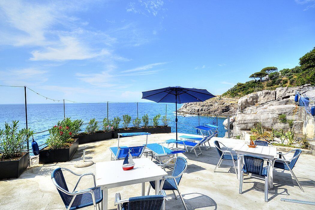 An outdoor seating area with tables and chairs, overlooking a body of water and rocky terrain.
