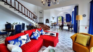Amplia sala de estar con un sofá rojo, un sillón amarillo y una escalera que sube a otro nivel.