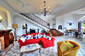 A spacious living room with a red sectional sofa, a yellow armchair, a chandelier, and a staircase leading to another level. - Villa Talassia: A charming two-story villa built sheer above the sea and with direct access to the sea, with Free WI-FI. (Massa Lubrense)