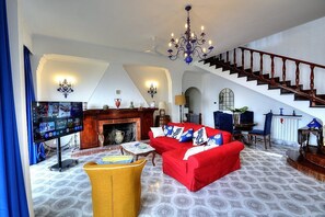 Ein großzügiger Wohnraum mit einem roten Sofa, einem gelben Sessel, einem Kamin, einem Fernseher und einer Treppe.