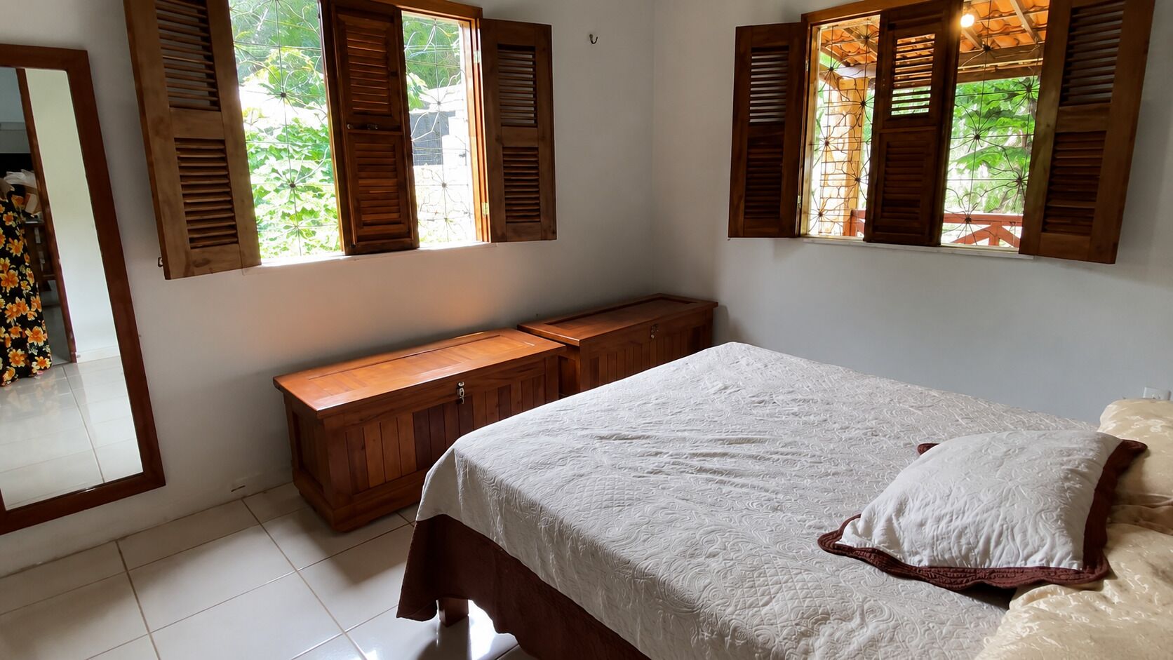Une chambre à coucher avec un lit, une armoire en bois et deux fenêtres équipées de volets.