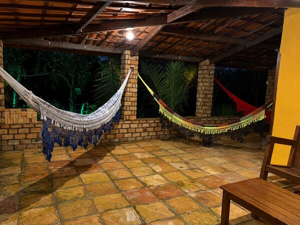 A covered outdoor area with two hammocks, a brick wall, and a tiled floor.