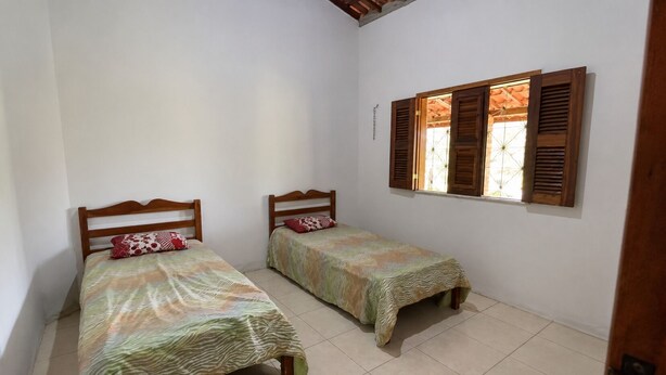 Une chambre avec deux lits simples, des têtes de lit en bois, une fenêtre avec des volets en bois et un sol carrelé.