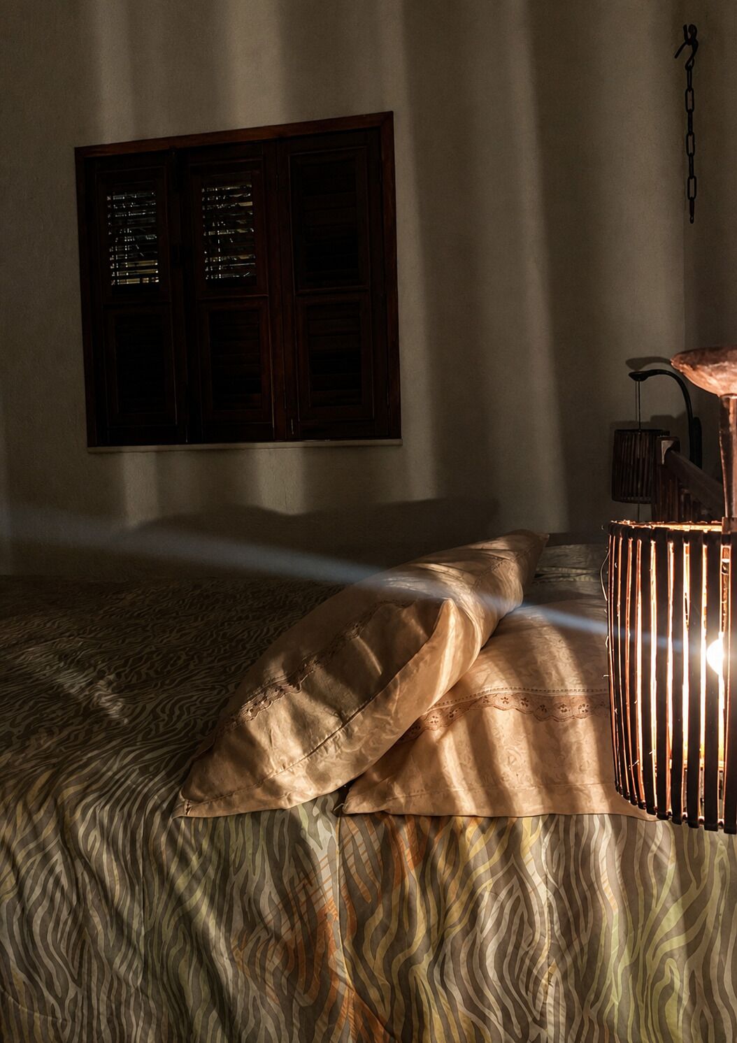 A bedroom with a bed, a window with blinds, and a lamp.