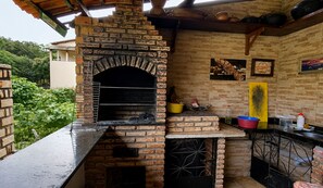 Forllat de maó a l'aire lliure amb una xemeneia, una barra amb un rentaplat i una prestatgeria amb diversos objectes de cuina.