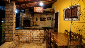 Une cheminée en briques, une table et des chaises en bois, un luminaire suspendu et un mur jaune.