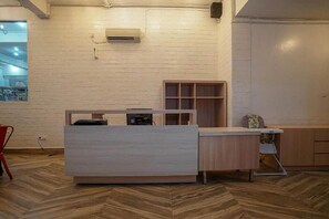 Mostrador de recepción con encimera blanca y panel de madera, una silla roja y suelo con estampado de espiga.