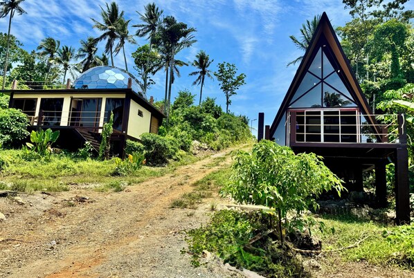 A tropical resort with a dirt path leading to a house with a glass dome and a triangular structure.