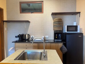 A compact kitchen with a stainless steel sink, a coffee maker, a kettle, a microwave, and a water dispenser.